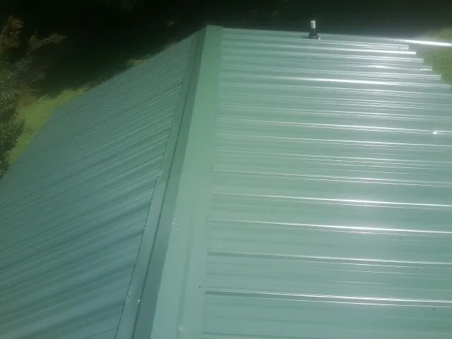 New green metal panels meeting at the ridge of a roof — Flat Roof Repair work by our crew in Feasterville Trevose