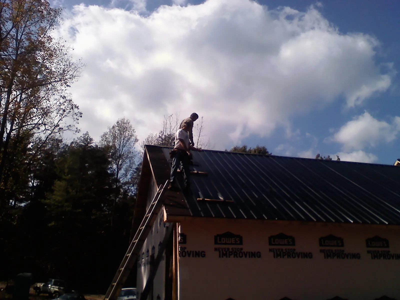 Roofer fastening dark metal panels high against a cloudy sky, from a Roof Inspection job in Feasterville Trevose