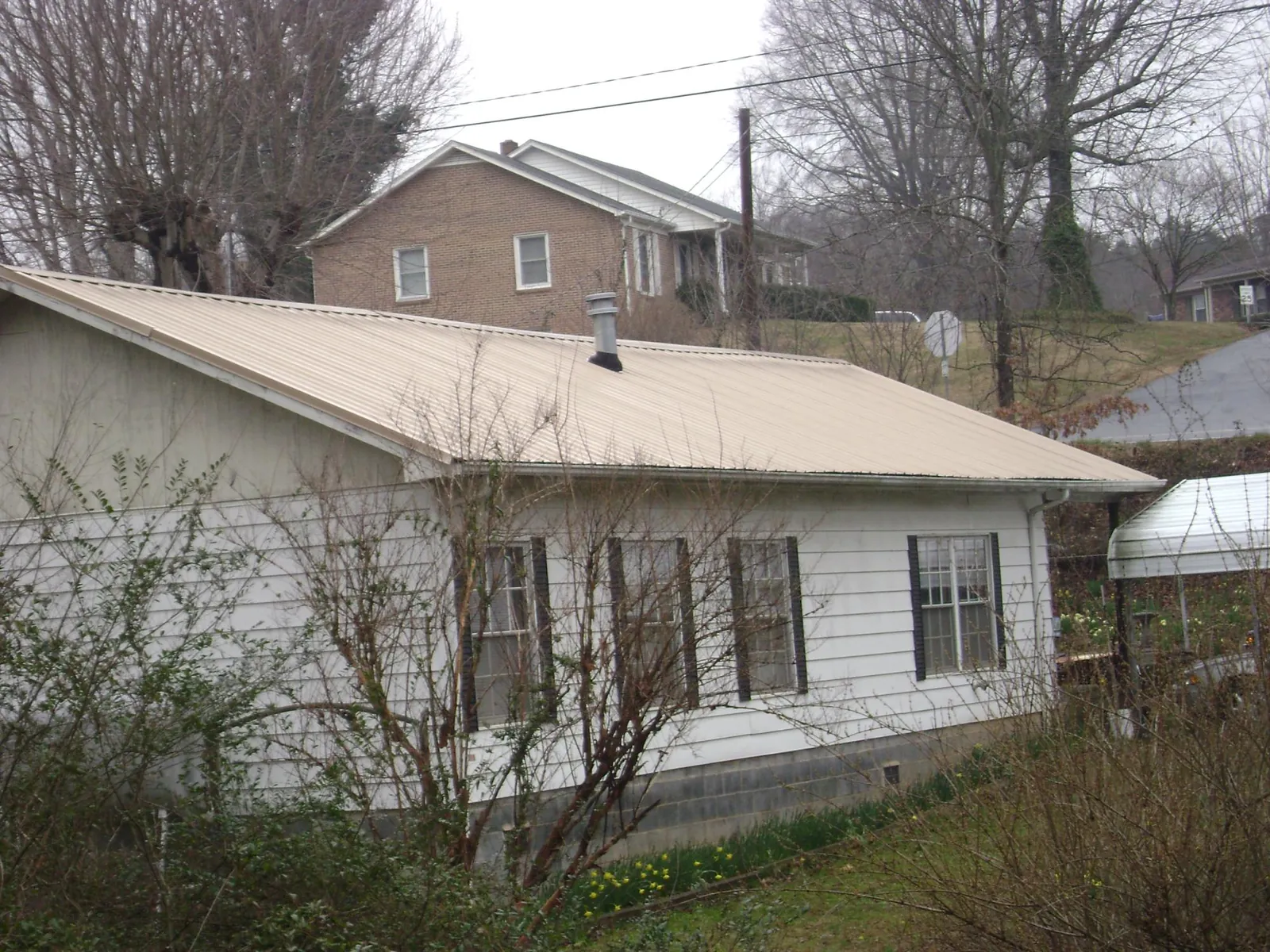 Tan metal roof on a white sided house set into a hillside — Commercial Roofing by Roofing Brothers in Feasterville Trevose