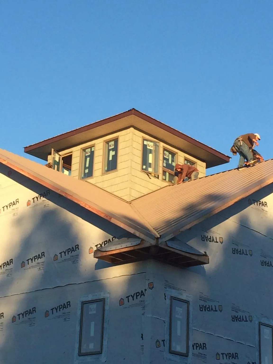 Roofers working around a rooftop cupola on a new metal roof at sunset in Feasterville Trevose
